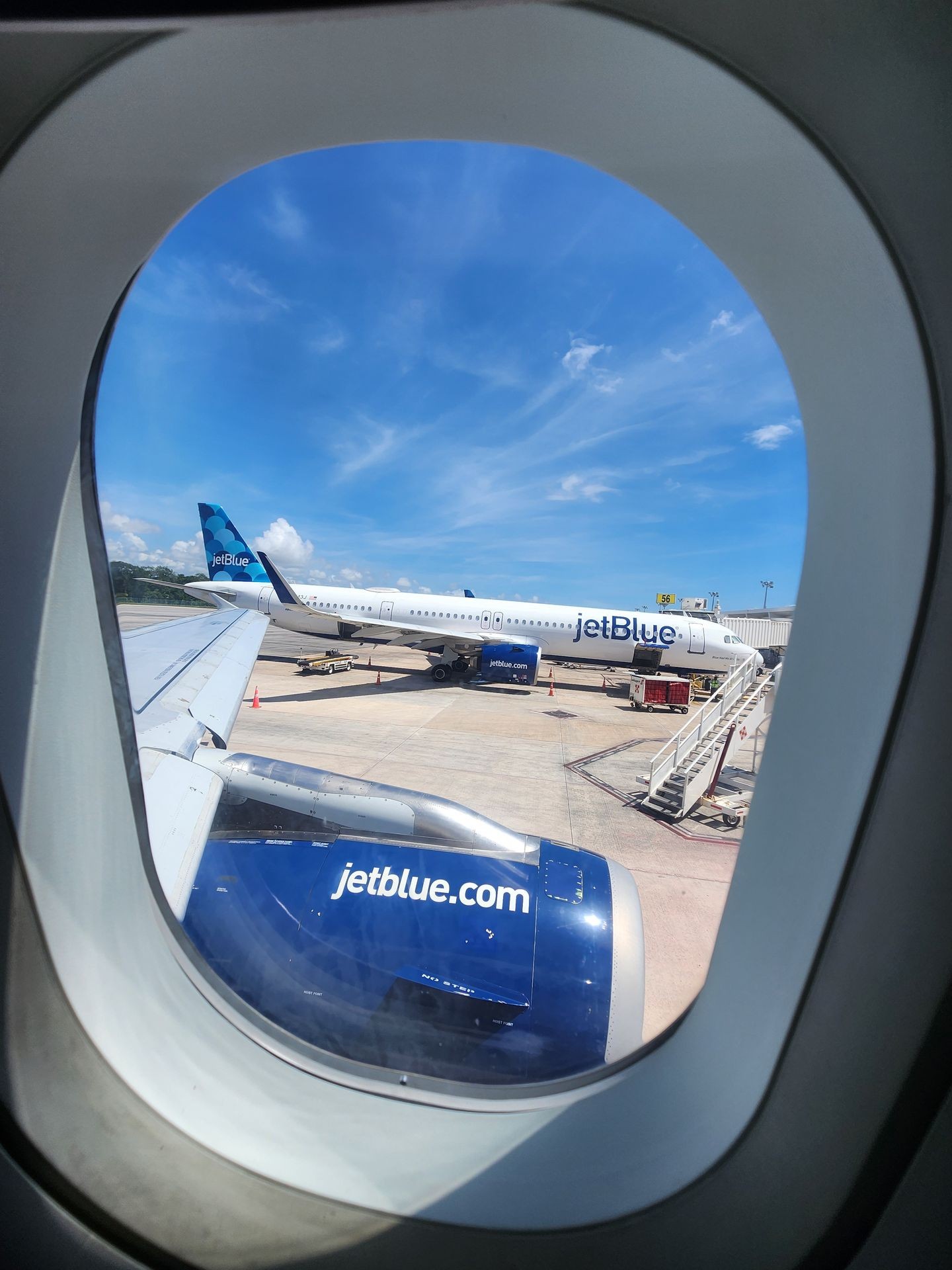 View from airplane window showing JetBlue plane on tarmac under blue sky.