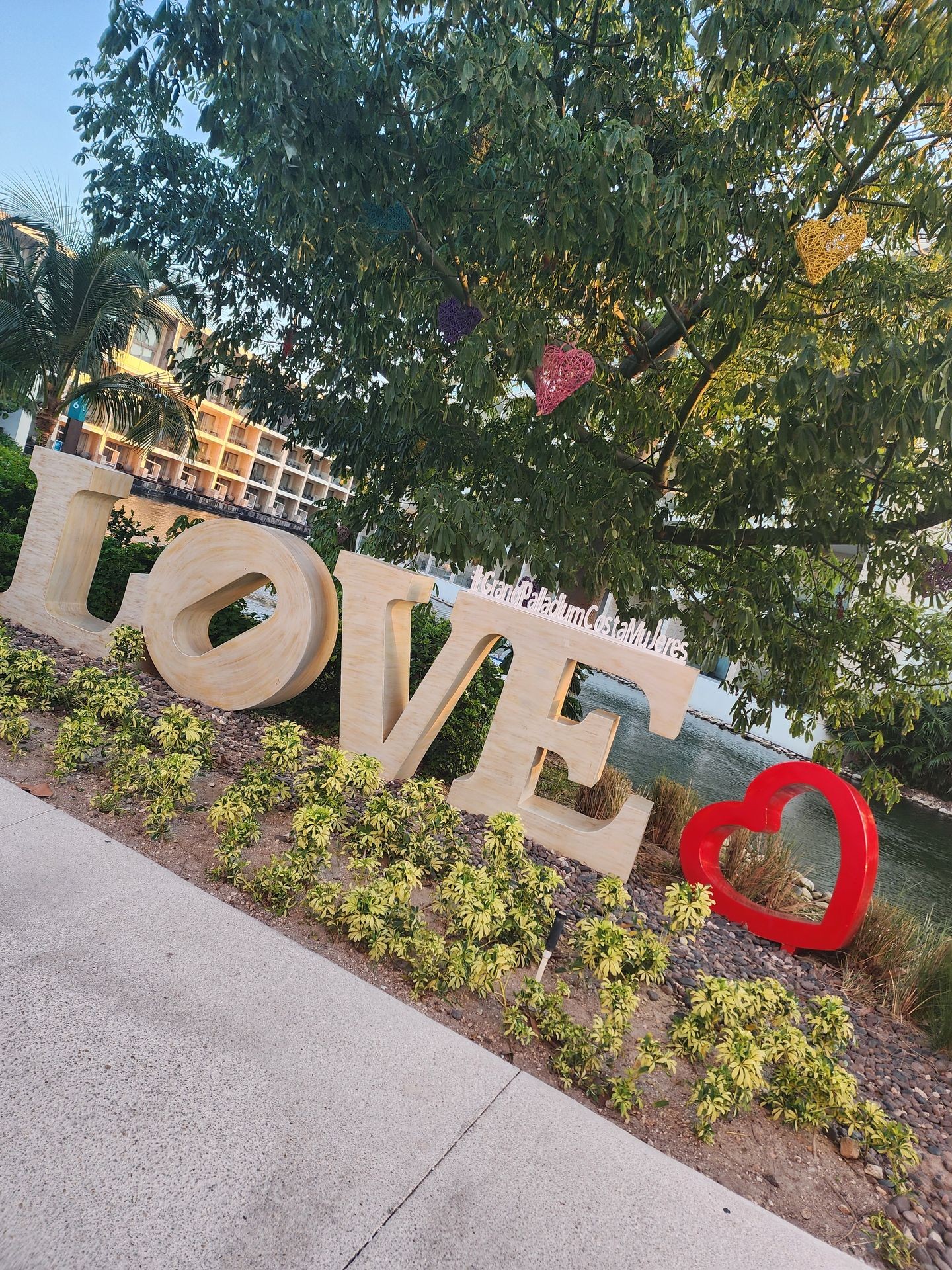 Large 'LOVE' sign in a garden setting with green plants and heart decorations in a tree.