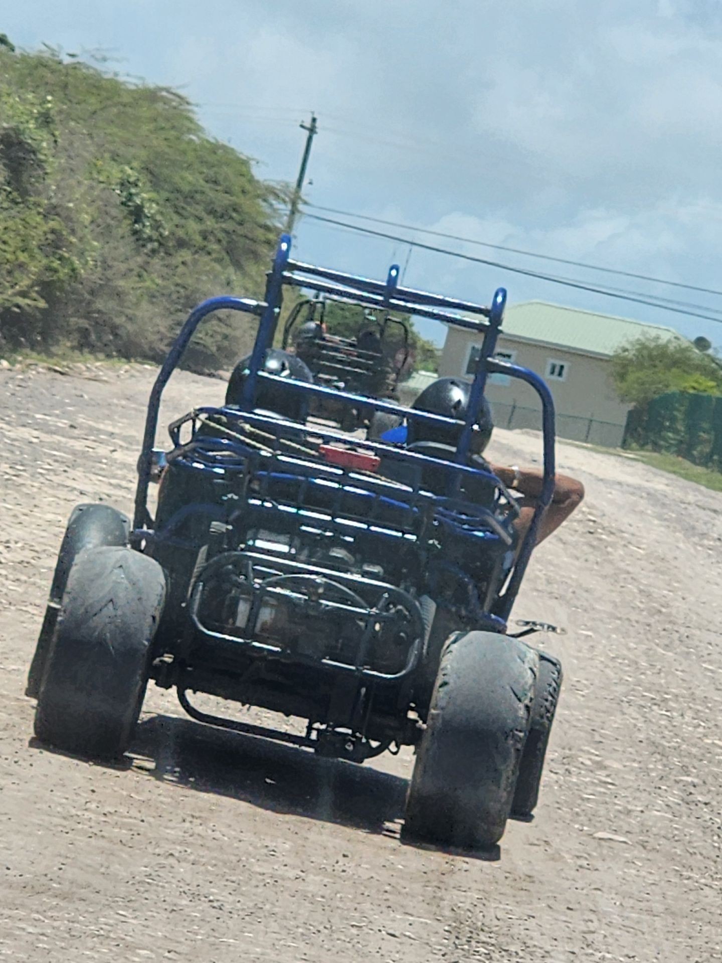 Rear view of a blue dune buggy with two passengers on a rocky dirt road.